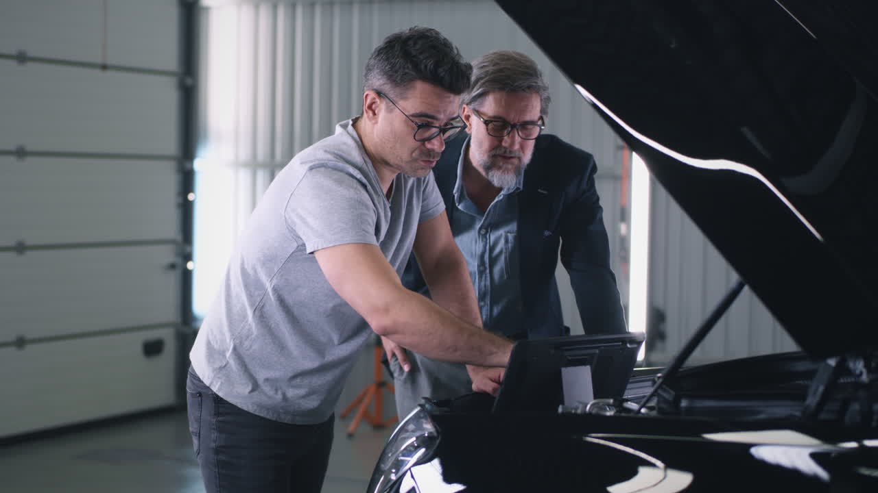 Two men inspecting a car engine with a diagnostic tool in a garage