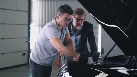 two men inspecting a car engine with a diagnostic tool in a garage
