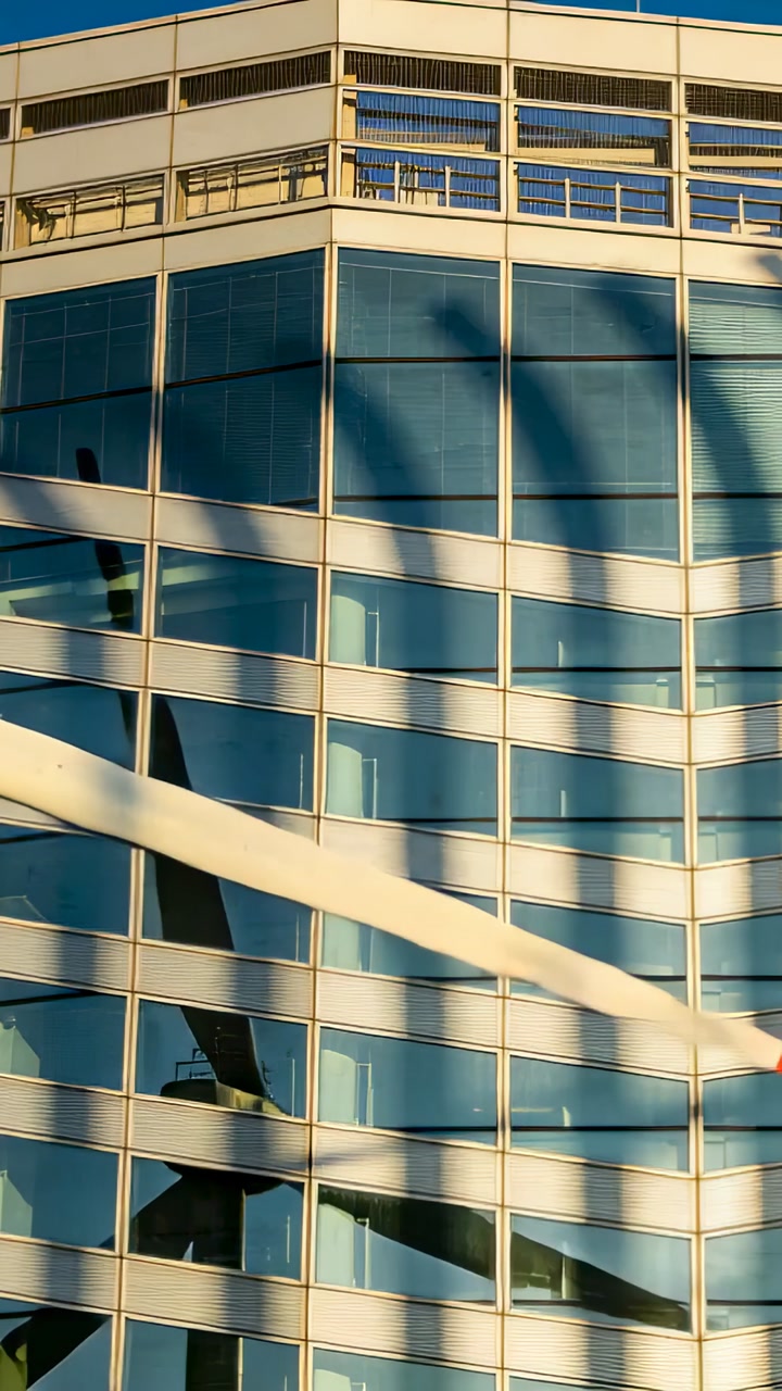 Vertical video: Moving ribbon entering left across downtown glass wall, showing arched shade in sun