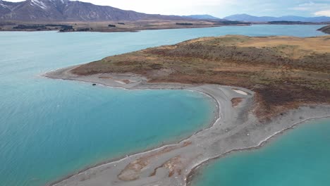 turquoise lake tekapo with sandy peninsula in canterbury, new zealand. aerial sideways shot