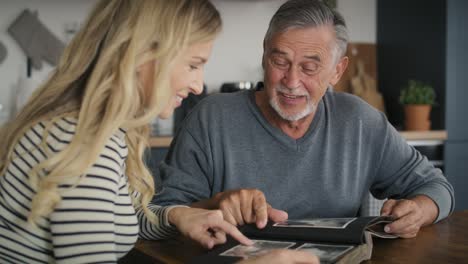 Senior-man-meeting-with-adult-daughter-and-looking-at-old-pictures-in-album.