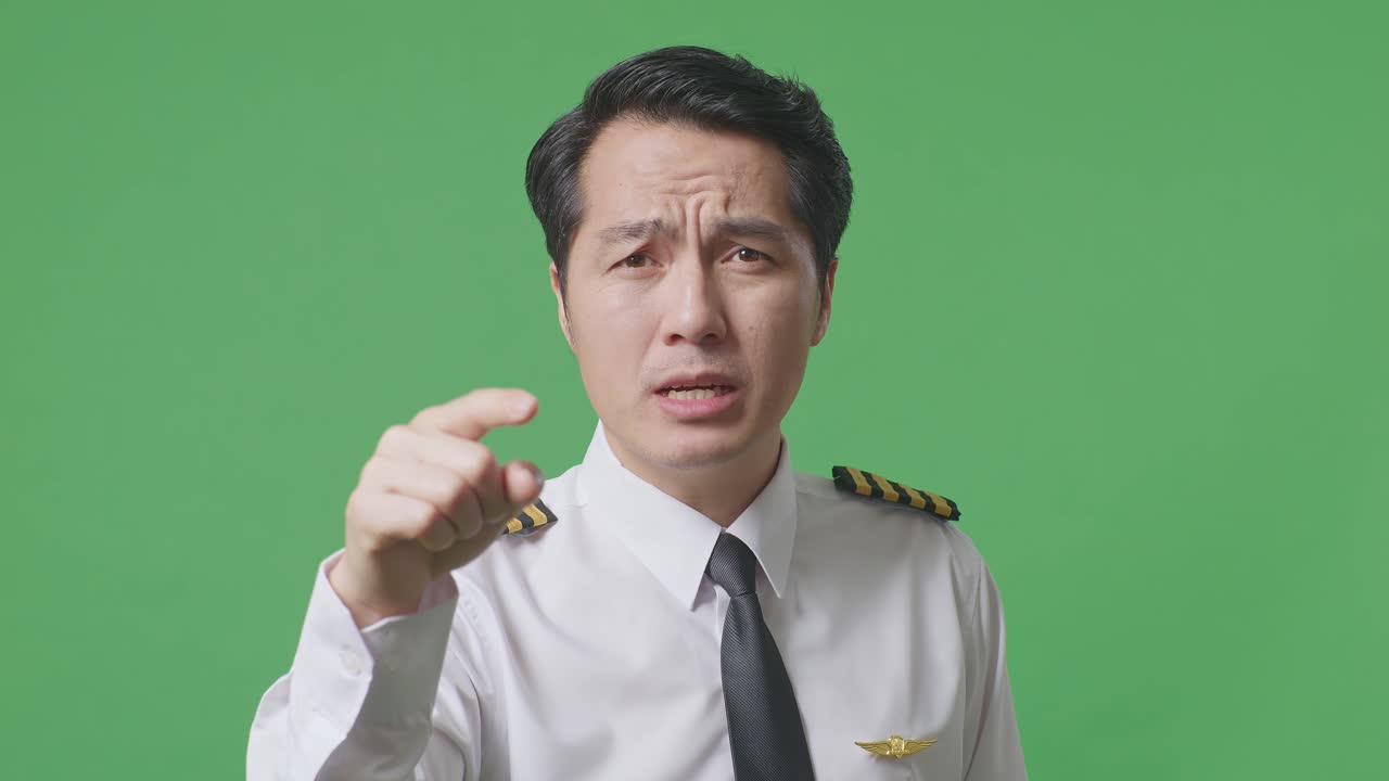 녹색 스크린 배경 스튜디오에 서 있는 동안 카메라에 소리치는 아시아 남자 조종사