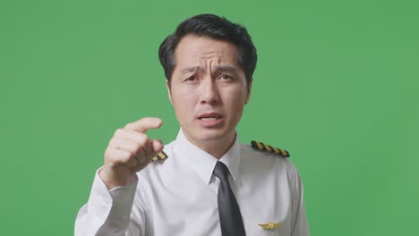 녹색 스크린 배경 스튜디오에 서 있는 동안 카메라에 소리치는 아시아 남자 조종사
