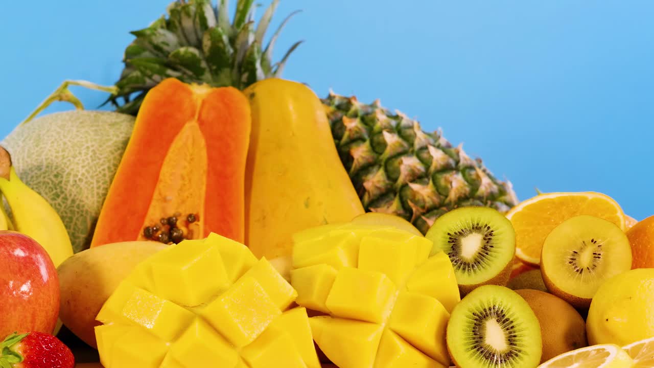 A colorful assortment of tropical fruits including papaya, pineapple, mango, and more against a blue background.