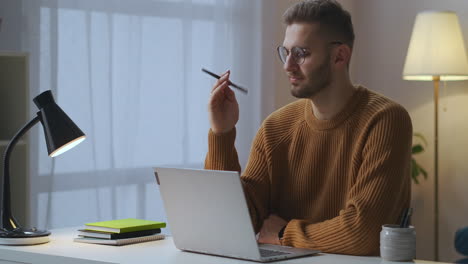 Ein-Nachdenklicher-Mann-Sitzt-Vor-Seinem-Laptop-Im-Zimmer-Und-Denkt,-Er-Hält-Einen-Stift-In-Der-Hand,-Ein-Freiberuflicher-Schriftsteller-Oder-Journalist-Arbeitet-Zu-Hause