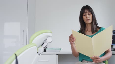 Portrait-of-biracial-female-patient-holding-documents-at-modern-dental-clinic