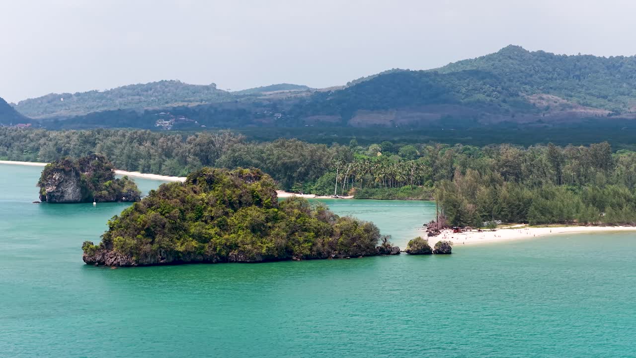 Wide aerial shot of turquoise water and lush limestone islands under bright daylight in Thailand