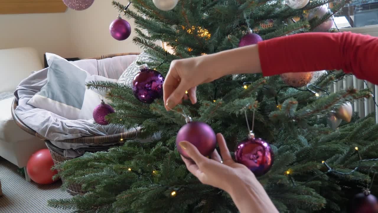 chica rubia adorna el árbol de navidad con bolas moradas.