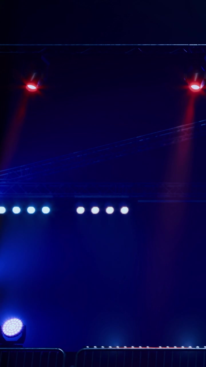 Bright lights shine at a stage during a nighttime event with a dark sky