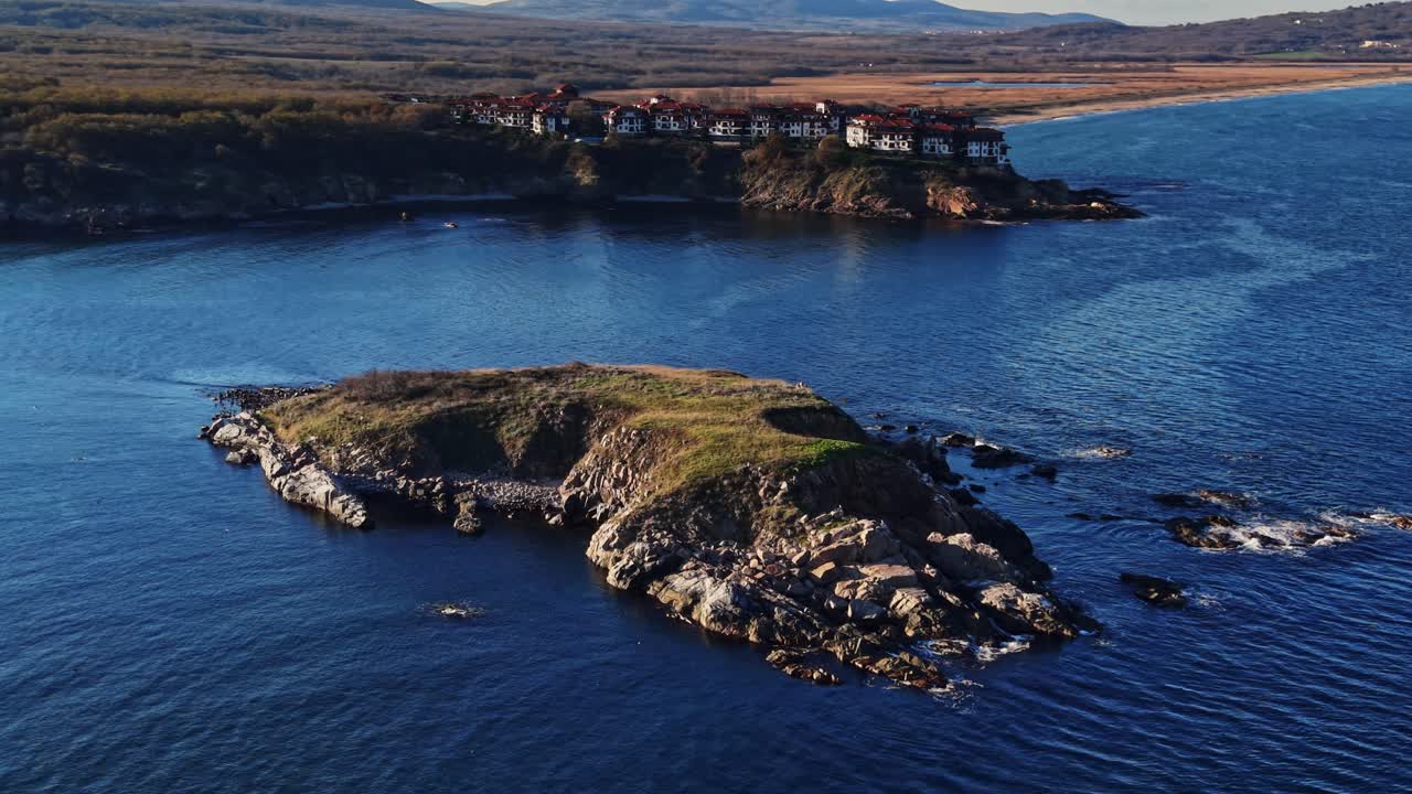 Dramatic aerial view of rocky island and coastal buildings at sunset