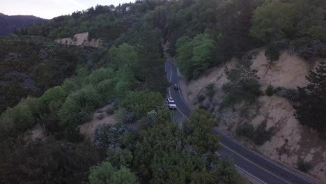 Dunkler-Geländewagen-Fährt-In-Der-Abenddämmerung-Auf-Einer-Zweispurigen-Autobahn-Durch-Einen-Bergkiefernwald-Um-Eine-Kurve