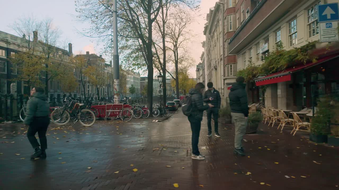 Tranquil view of an Amsterdam canal lined with autumn trees and bicycles. Historic buildings and soft morning light create a peaceful urban atmosphere. Location: Amsterdam, Nederland Travel to left