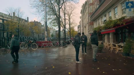 tranquil view of an amsterdam canal lined with autumn trees and bicycles. historic buildings and soft morning light create a peaceful urban atmosphere. location: amsterdam, nederland travel to left