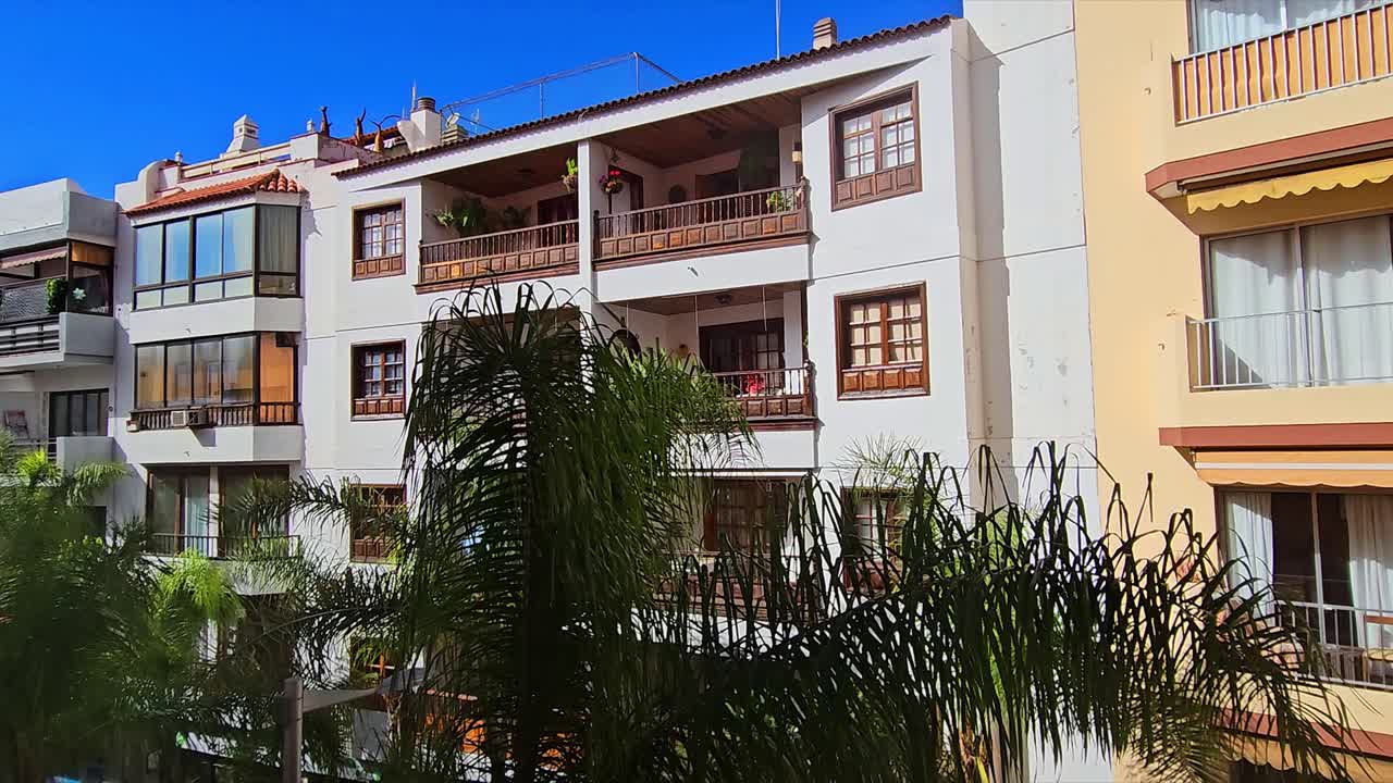 Apartment building with balconies and green palm trees in Puerto, Spain