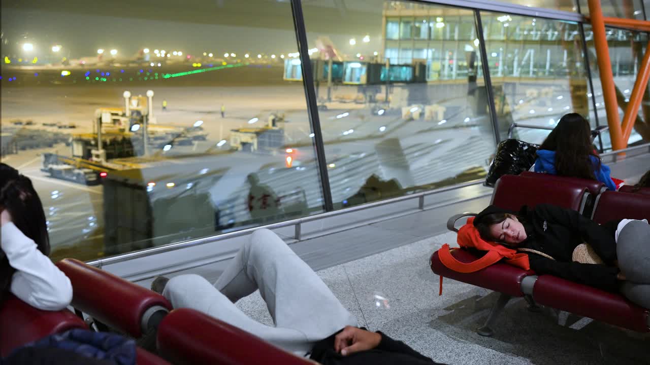 During the night, passengers relax on benches near the boarding gate, awaiting their flight at Beijing International Airport, China.