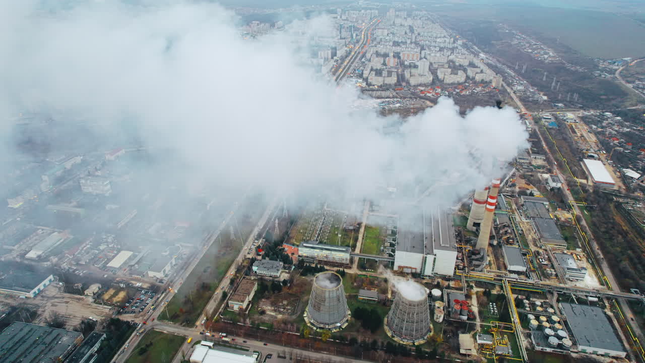 Aerial drone view of thermal power plant in Chisinau at cloudy weather, Moldova. View of pipes with felling steam, buildings and yellowed trees around