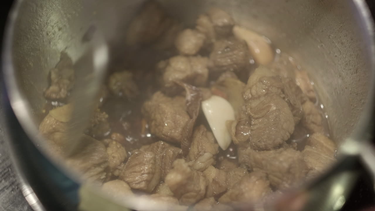 찐 삼겹살과 마늘을 꼬투리에서 요리하고 금속 스푼으로 저어줍니다.