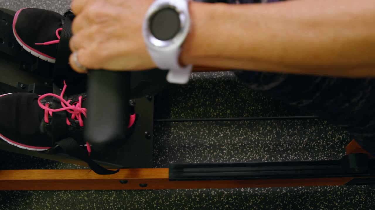 Senior woman exercising on water rowing machine in fitness studio 4k