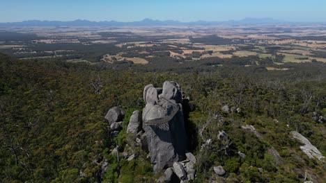 Antena-De-Un-Mirador-Hecho-Por-El-Hombre-En-Lo-Alto-De-Una-Roca-Gigante-En-Un-Arbusto-Australiano,-Montañas-En-El-Fondo