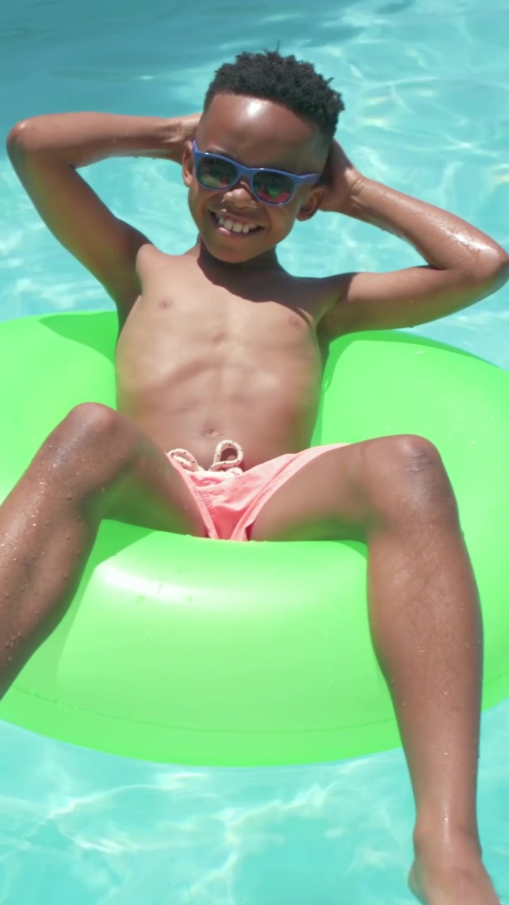 Vertical video: Drifting current, boy in pink trunks sliding right at pool, green ring, copy space