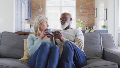 mixed race senior couple drinking coffee together while sitting on the couch at home