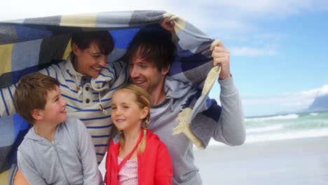 happy family hiding in blanket at beach