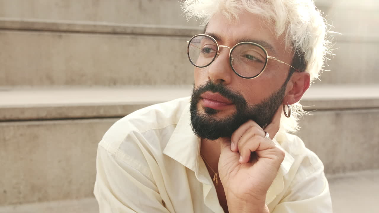 Thoughtful Man with Blonde Hair and Glasses Sitting Outdoors