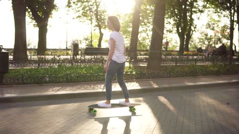 young woman in blue jeans and white sneakers skateboarding at sunrise in park. legs on the skateboard. slow motion shot