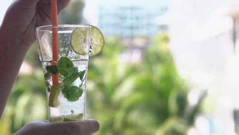 girl stirs slowly mojito cocktail with long orange straw