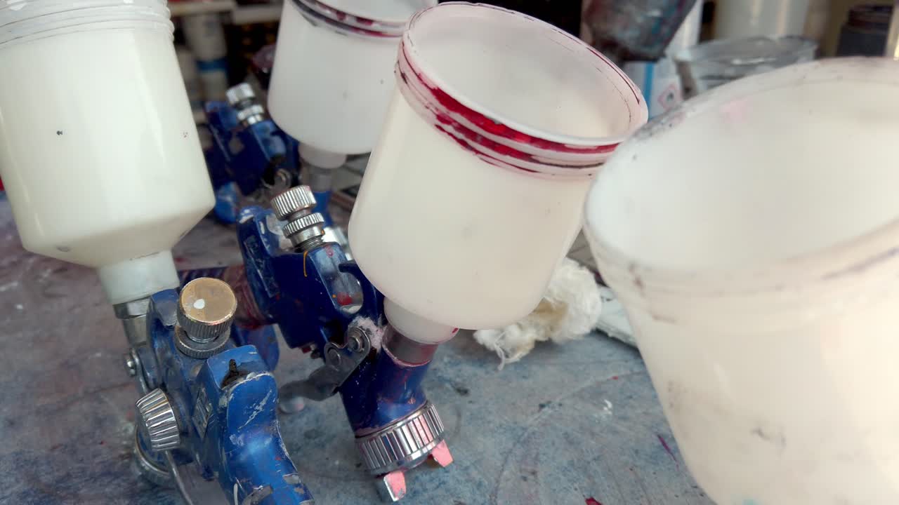 Close-up of paint sprayer with three white paint cups in workshop