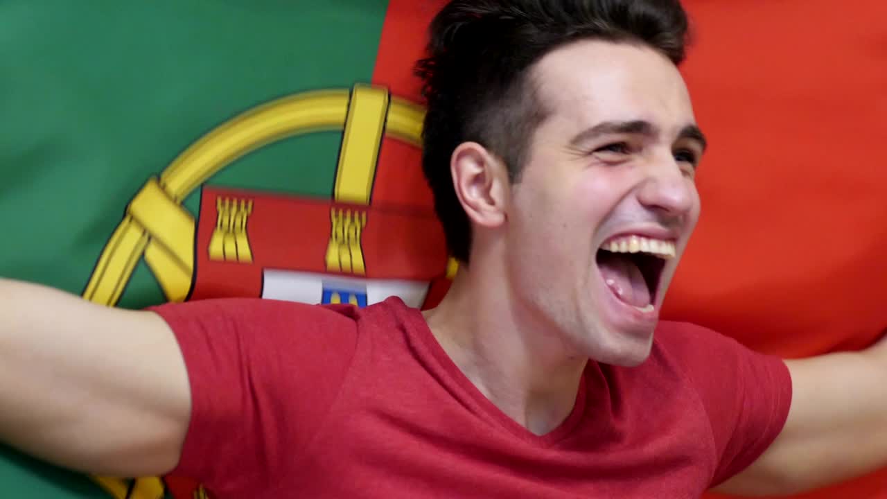 joven portugués celebrando mientras sostiene la bandera de portugal en cámara lenta