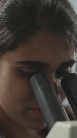 indian woman adjusts microscope to look at bacteria on blurred background. young student learns to use equipment in medical laboratory closeup