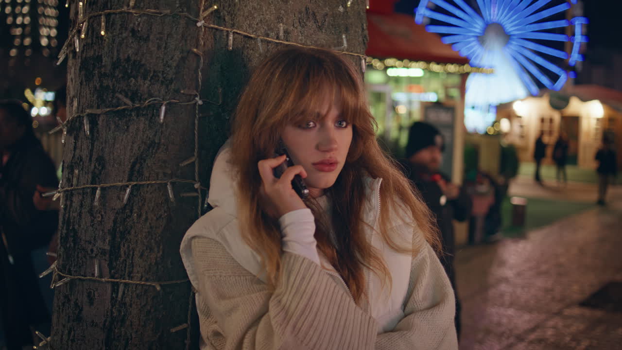 긴장한 여자가 휴대전화로 축제 거리의 클로즈업에서 이야기합니다. 밤을 부르는 여자