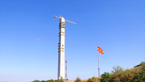 big concrete tower in construction with a crane on it and the macedonian flag