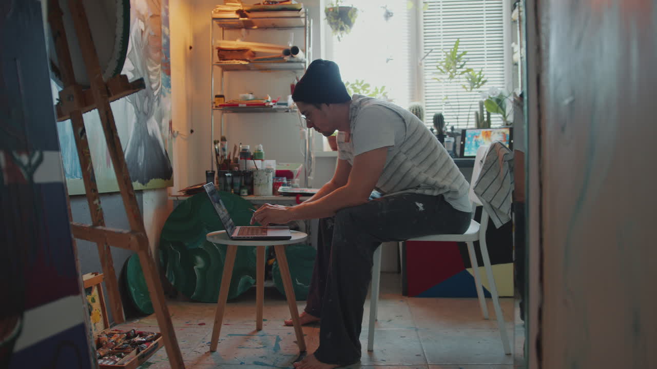 Professional Painter Using Laptop during Workday in Creative Studio
