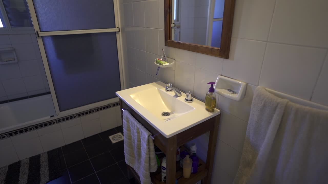 Crisp monochrome bathroom featuring glossy white walls, black floor, and a glass shower enclosure. Hand towel adds functional detail. Ideal for modern rental listings.