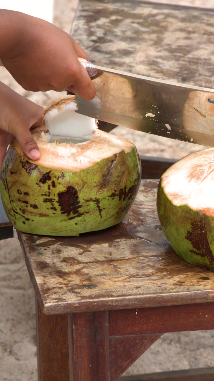 Close-up of Hands Opening a Fresh Green Coconut with a Machete