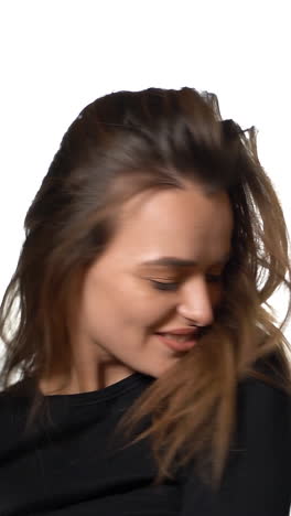 pretty woman with long hair is turning around and posing for the camera in the studio on a white background. close-up vertical video
