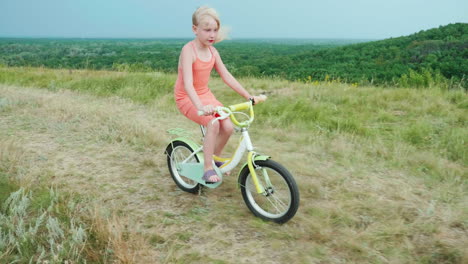 a cool girl in a pink dress rides a bike in the countryside 1