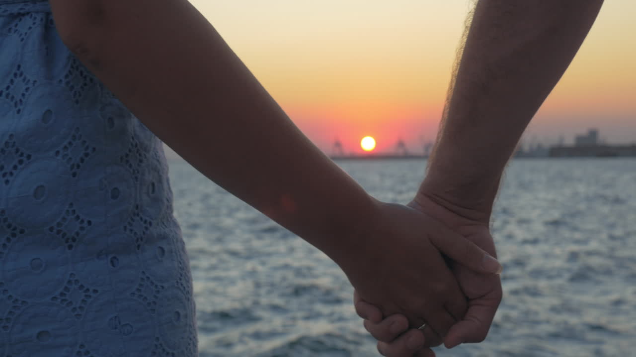 해가 지는 동안 해변에서 손을 잡고 있는 만적인 커플의 클로즈업  (piraeus, greece)