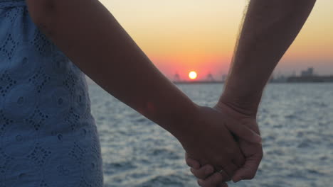 Primer-Plano-De-Una-Pareja-Romántica-Tomados-De-La-Mano-En-La-Playa-Contra-El-Atardecer-Pireo,-Grecia