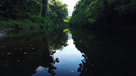 wide-view-of-water-flowing-down-dark-creek-with-sky-reflection-on-water