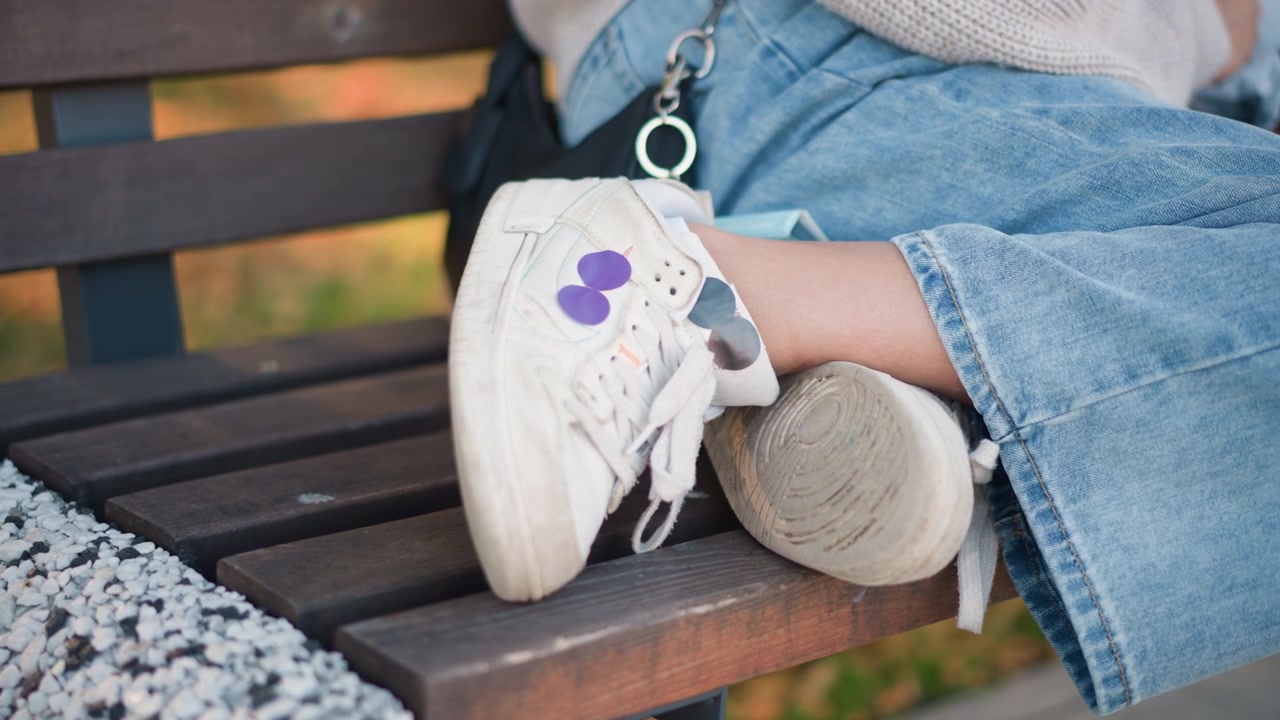 Persona seduta su una panchina del parco che indossa sneakers casual e jeans