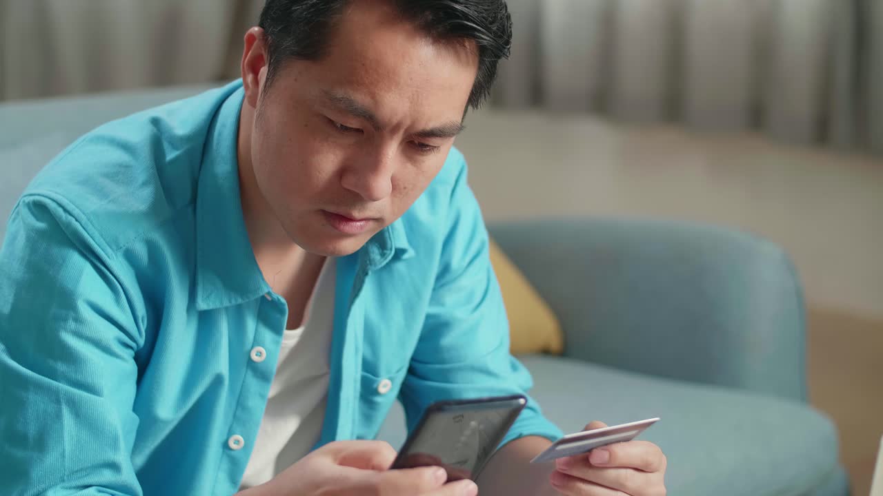 신용카드와 스마트폰을 들고 있는 노트북을 가진 아시아인 남자가 돈을 지불할 수 없어서 머리를 흔들고 있다.