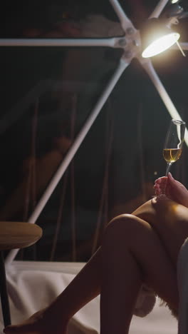una joven molesta bebe una bebida alcohólica en un vaso sentada en un sillón por la noche en una habitación de hotel brillante. sentimiento desagradable de soledad y devastación