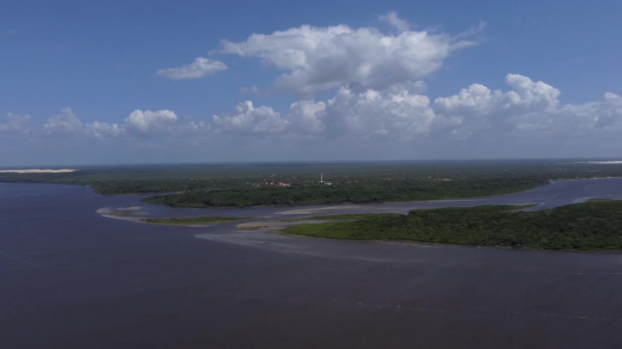 Brezilya'nın Maranhão eyaletinde, bir tarafında nehir diğer tarafında okyanus olan dar Caburé kum setindeki küçük rustik köy yapılarını yakalayan yüksek açılı drone çekimi.