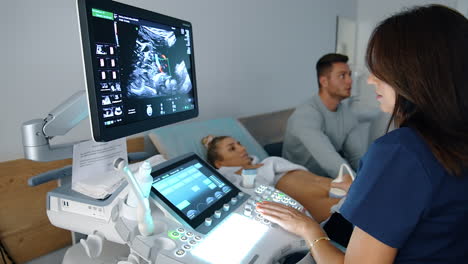 doctor sits at ultrasound machine. obstetrician checks the baby's development in the abdomen. happy couple at backdrop.