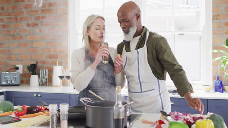 Mixed-race-couple-wearing-aprons-cooking-together-in-the-kitchen-at-home