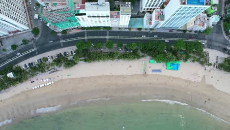 aerial top down view of the nha trang coastline flying parallel to the coastal road and white sand beach with large residential buildings facing the ocean and traffic driving along the road