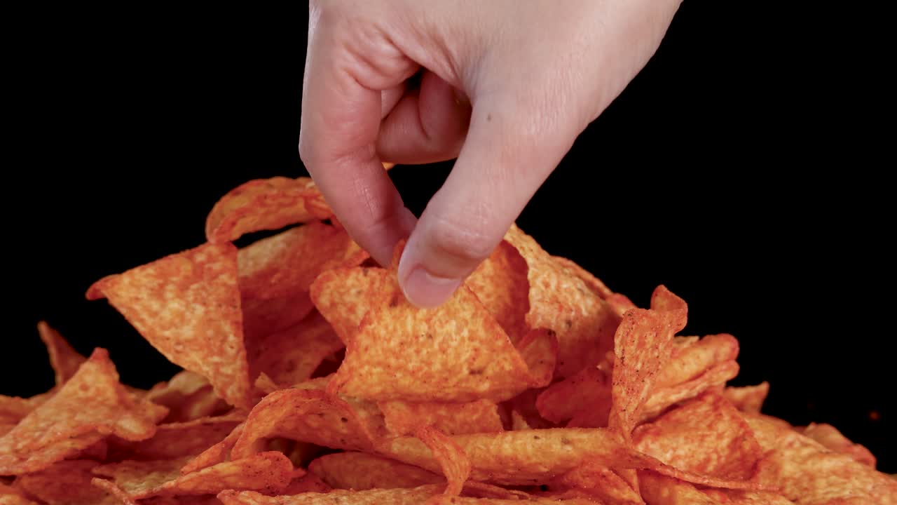 Una mano umana seleziona una tortilla chip da una pila sotto una luce brillante e uniforme, sfondo nero